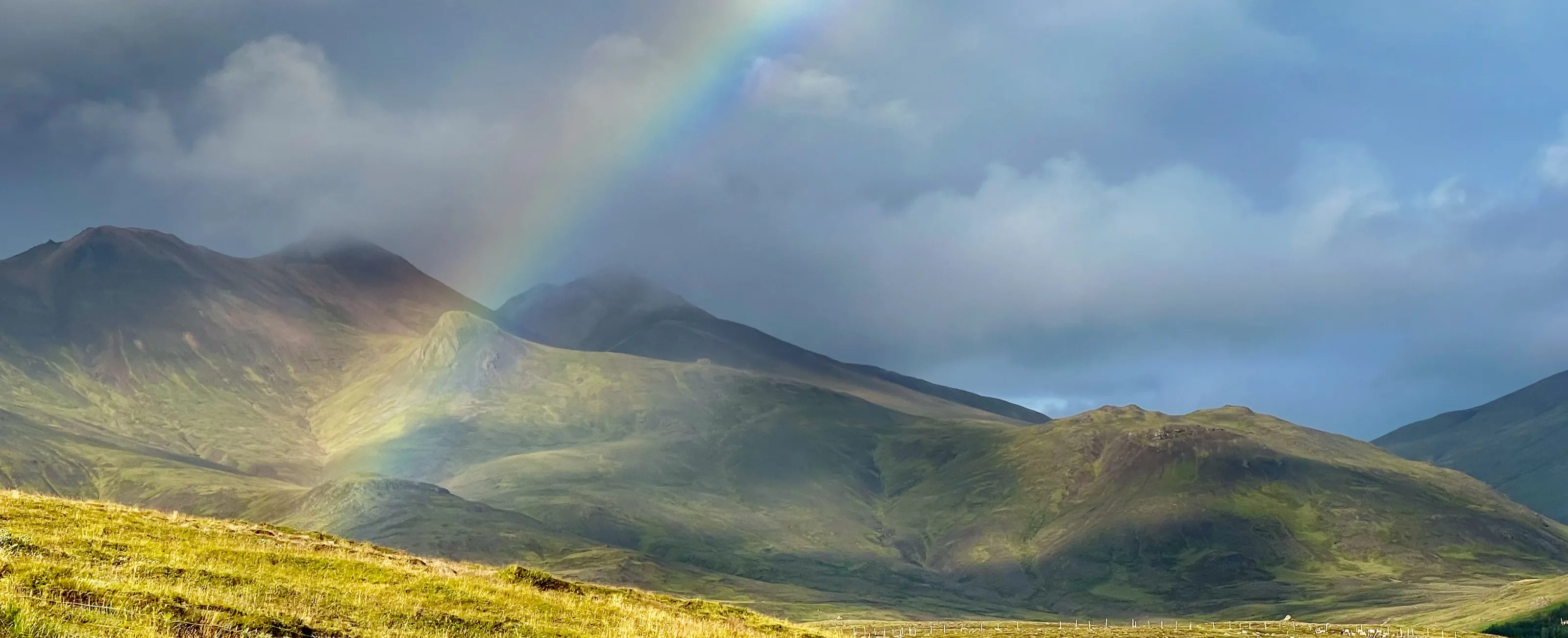 Rainbow over moss-green slopes in the capital region