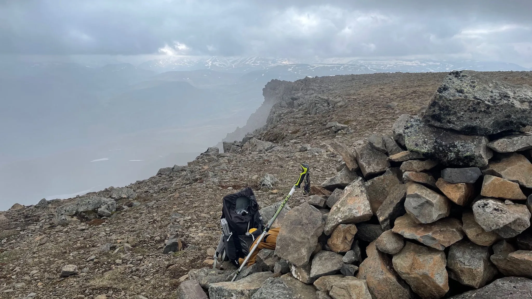 A pack and walking poles resting against a stone cairn in fog
