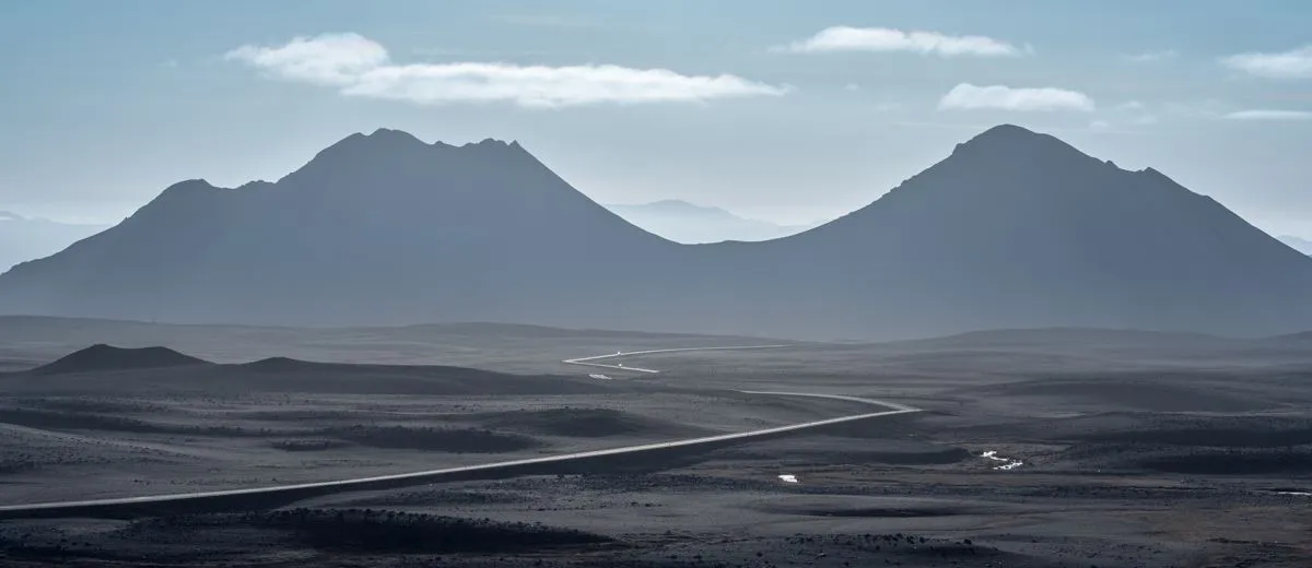 Empty road running across a black desert toward layered blue ridges