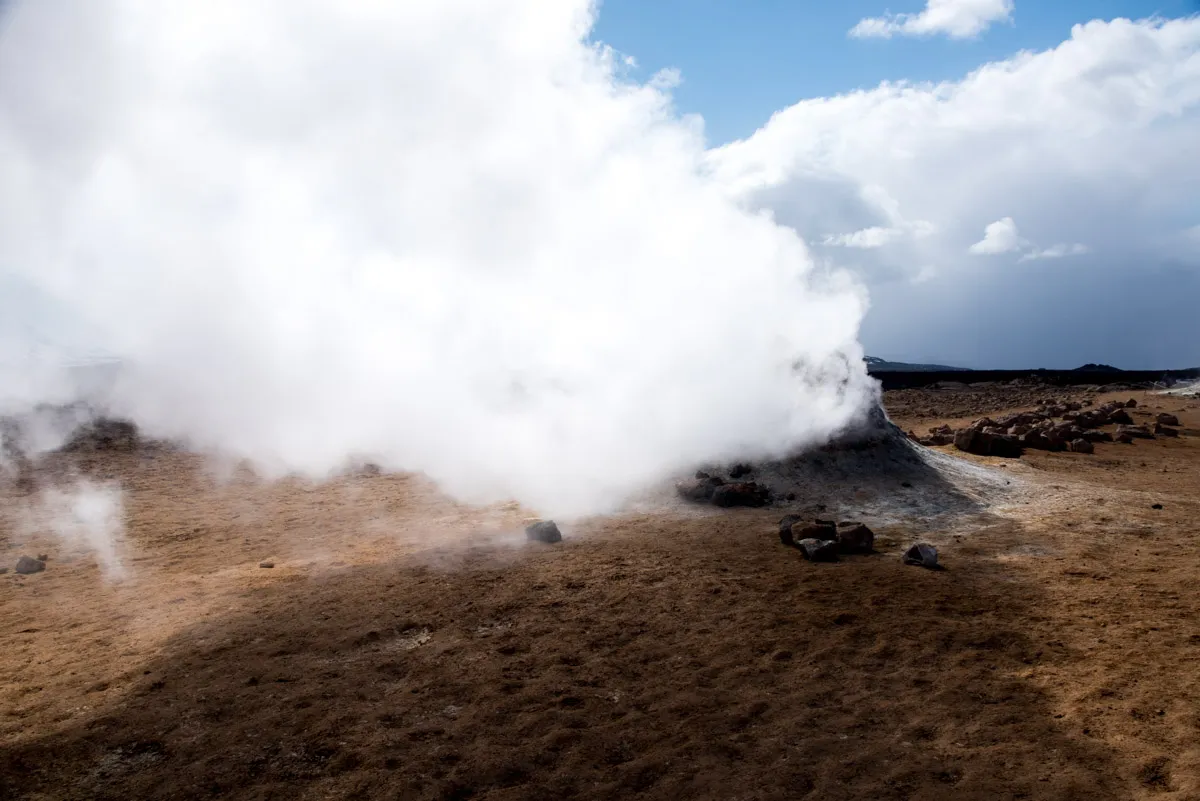 A fumarole venting a dense column of steam over bare ochre ground