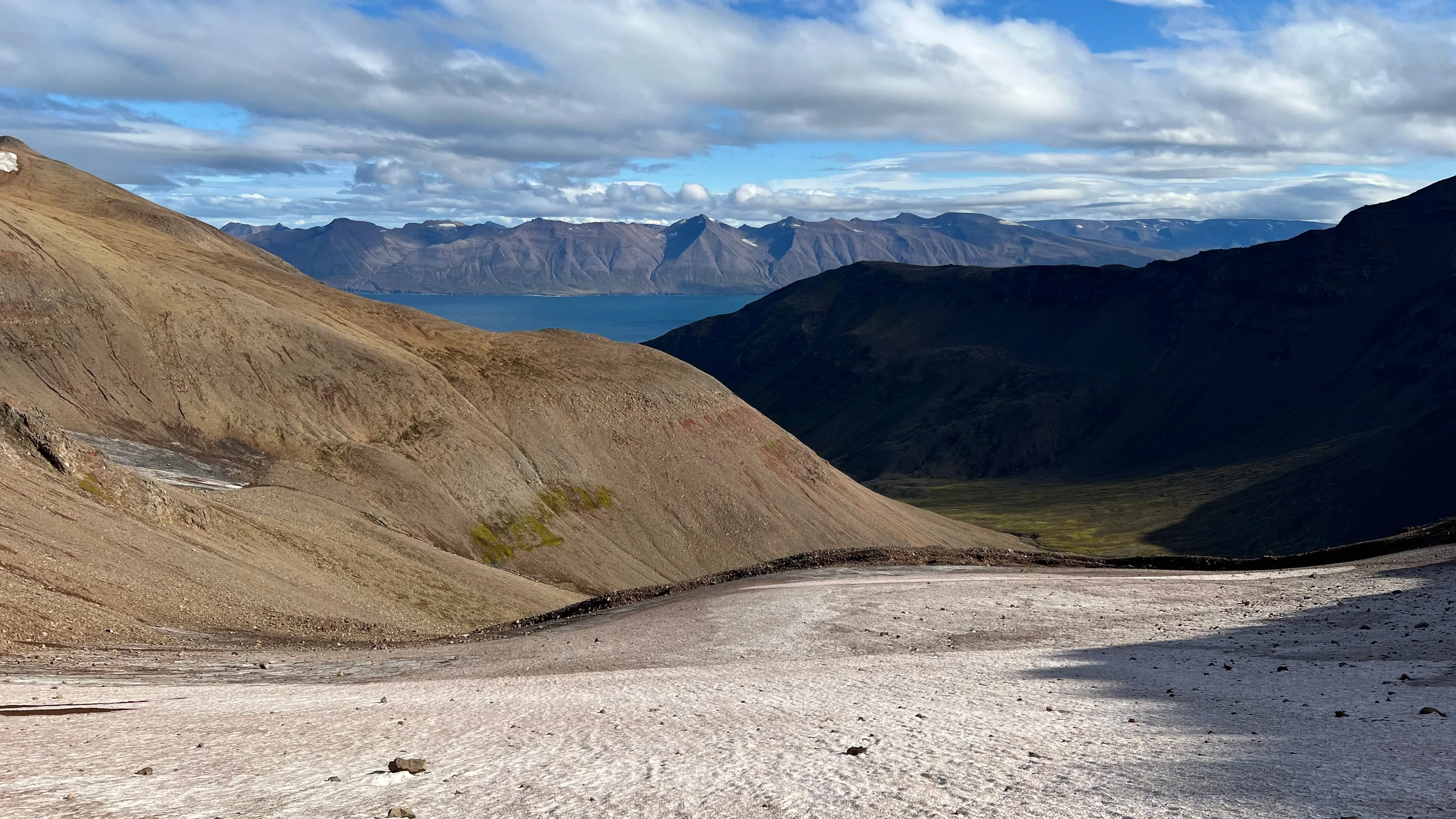 Looking back down a debris-dotted cirque glacier toward a fjord far below