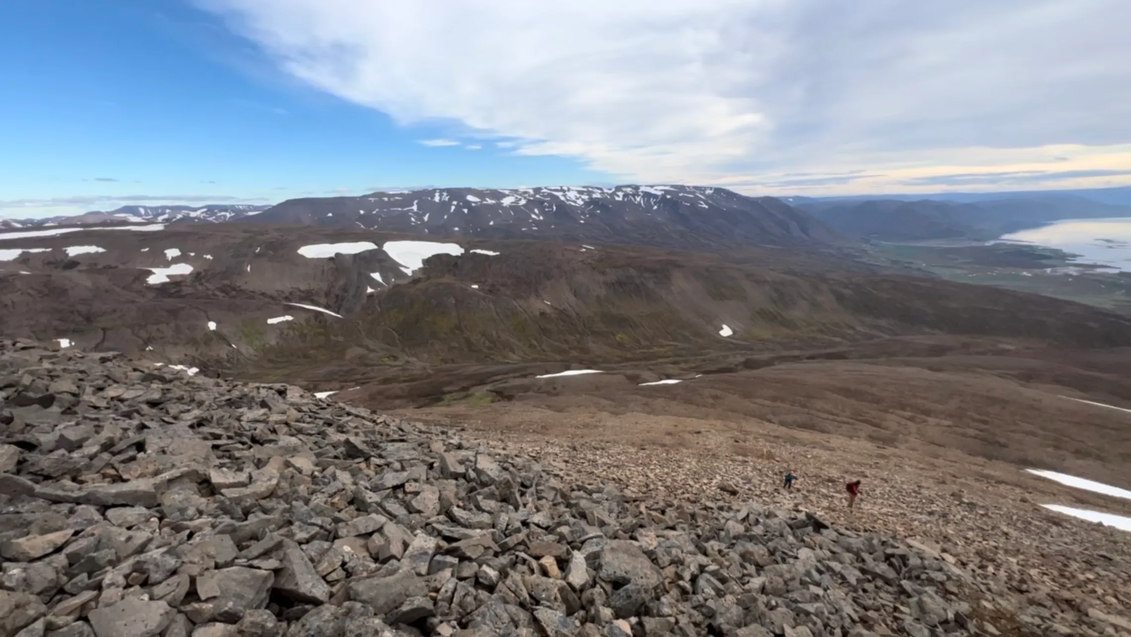 Two hikers picking their way up a vast blocky boulder field high above a fjord