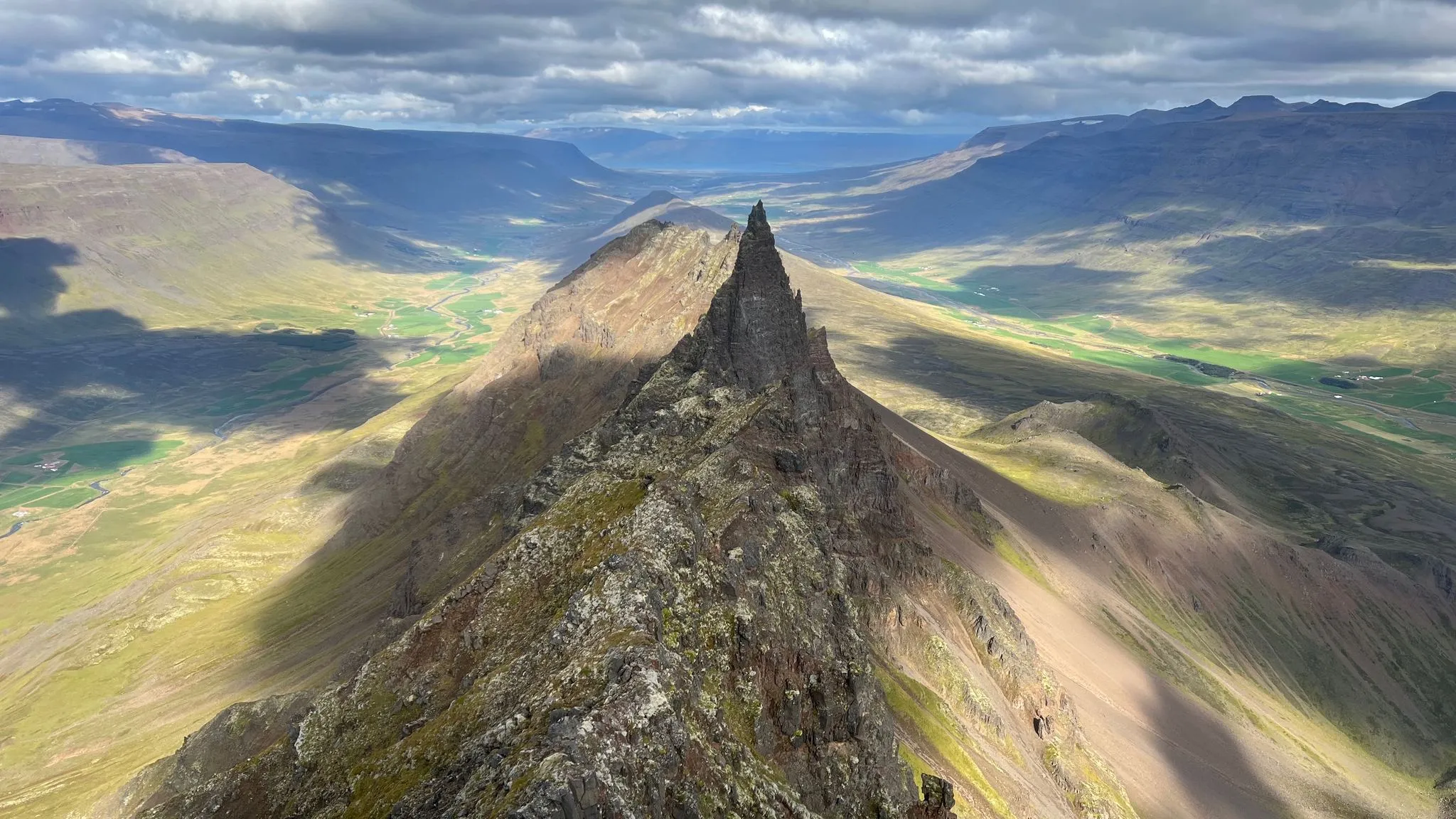 A knife-edged green ridge seen from above, valleys falling away on both sides toward the sea