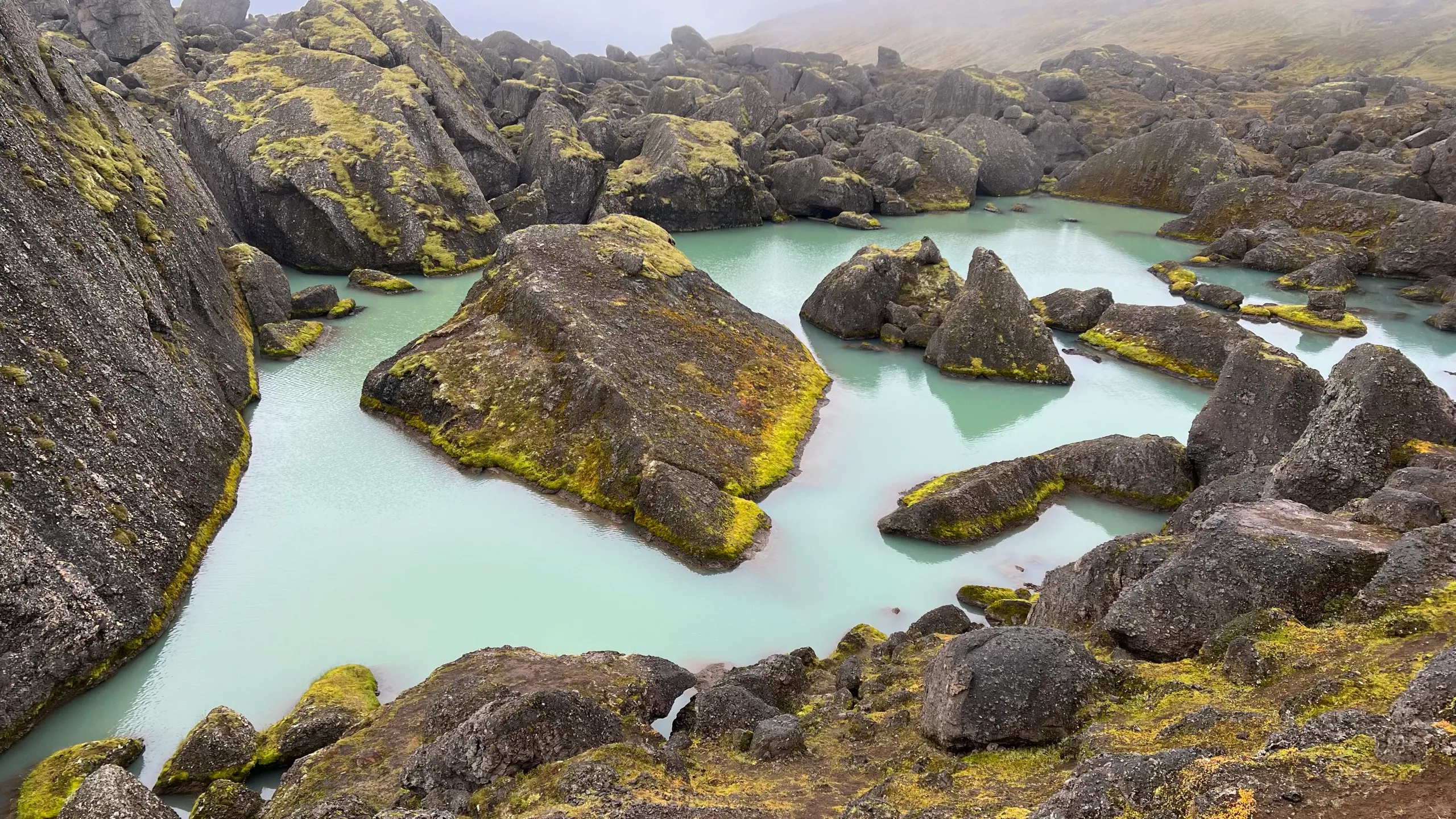 Turquoise pools between giant moss-covered boulders in the Stórurð basin